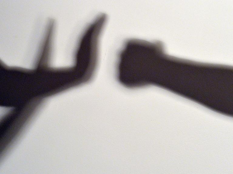 Gestelltes Bild zum Thema häusliche Gewalt - Schatten symbolisieren, wie eine Person sich vor der Gewalt einer anderen schützt.