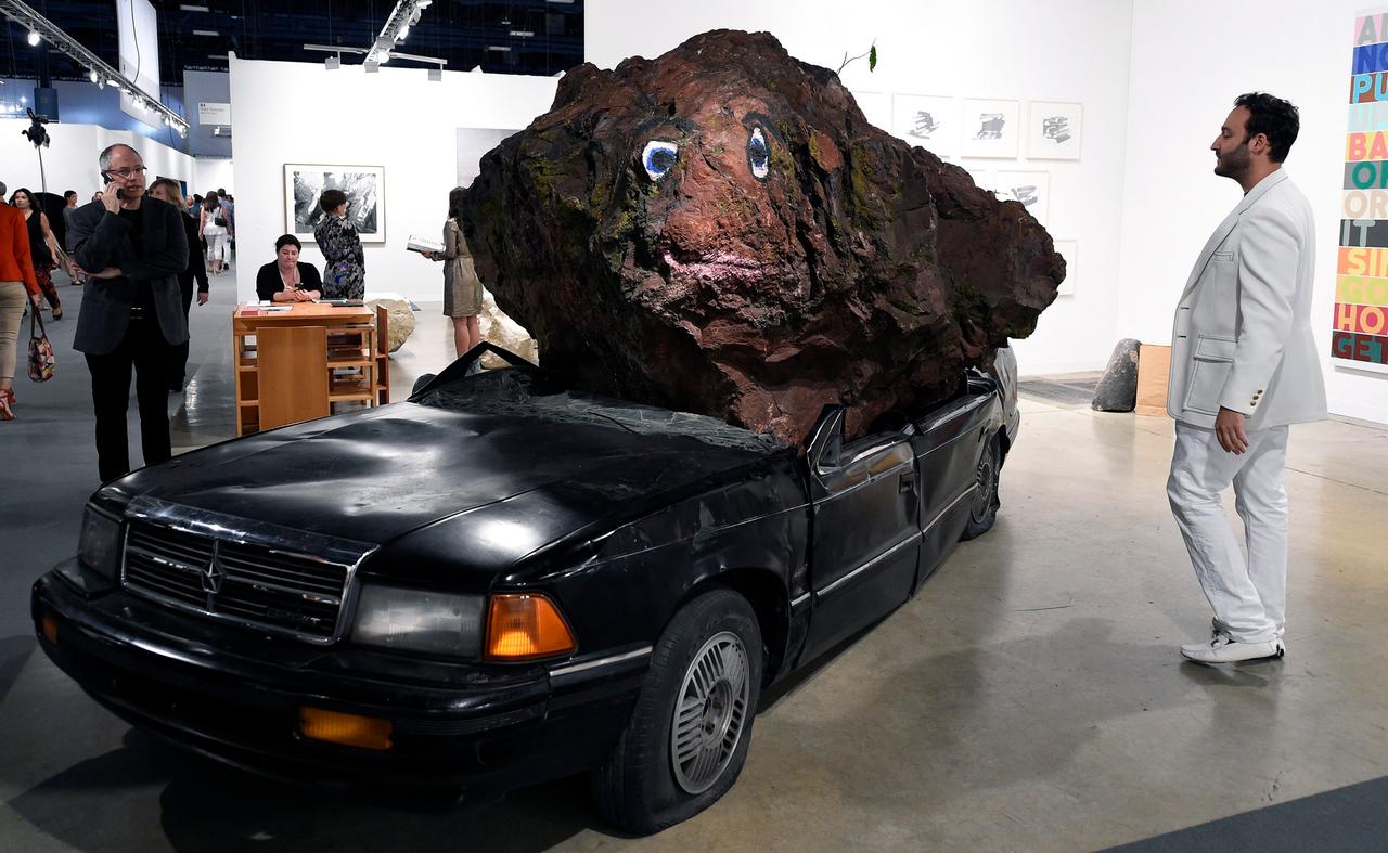 Ein großer brauner Steinbrocken liegt auf dem eingedrückten Dach einer schwarzen Limousine.