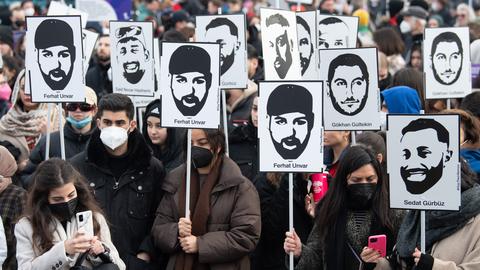 Mit Plakaten und Bildern der Ermordeten erinnern Teilnehmer einer Gedenkveranstaltung auf dem Marktplatz von Hanau an die Opfer der rassistisch motivierten Anschläge von Hanau im Jahr 2020.