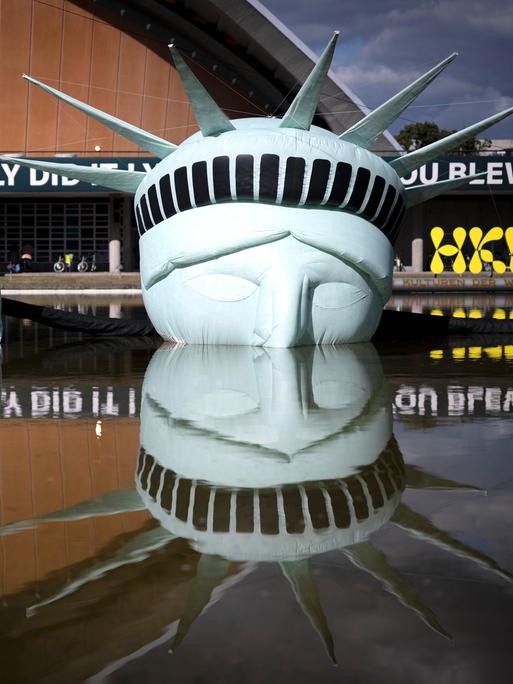 Eine halb versunkene, aufblasbare Replik der Freiheitsstatue liegt im Wasserbecken vor dem Haus der Kulturen der Welt in Berlin. 

