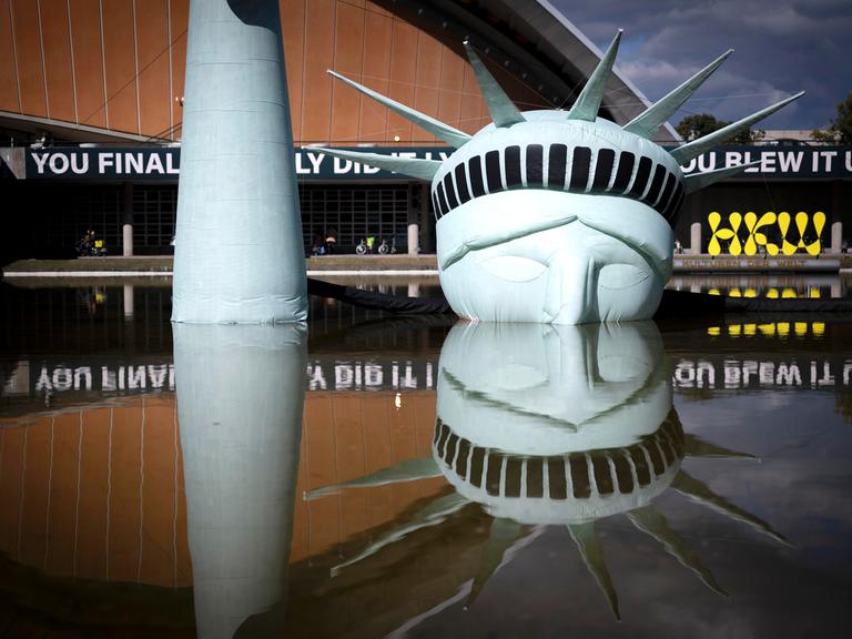 Eine halb versunkene, aufblasbare Replik der Freiheitsstatue liegt im Wasserbecken vor dem Haus der Kulturen der Welt in Berlin. 

