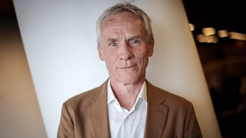 Ewald Frie steht im weißen Hemd und hellbraunen Sacko vor einer weißen Säule und schaut freundlich in die Kamera