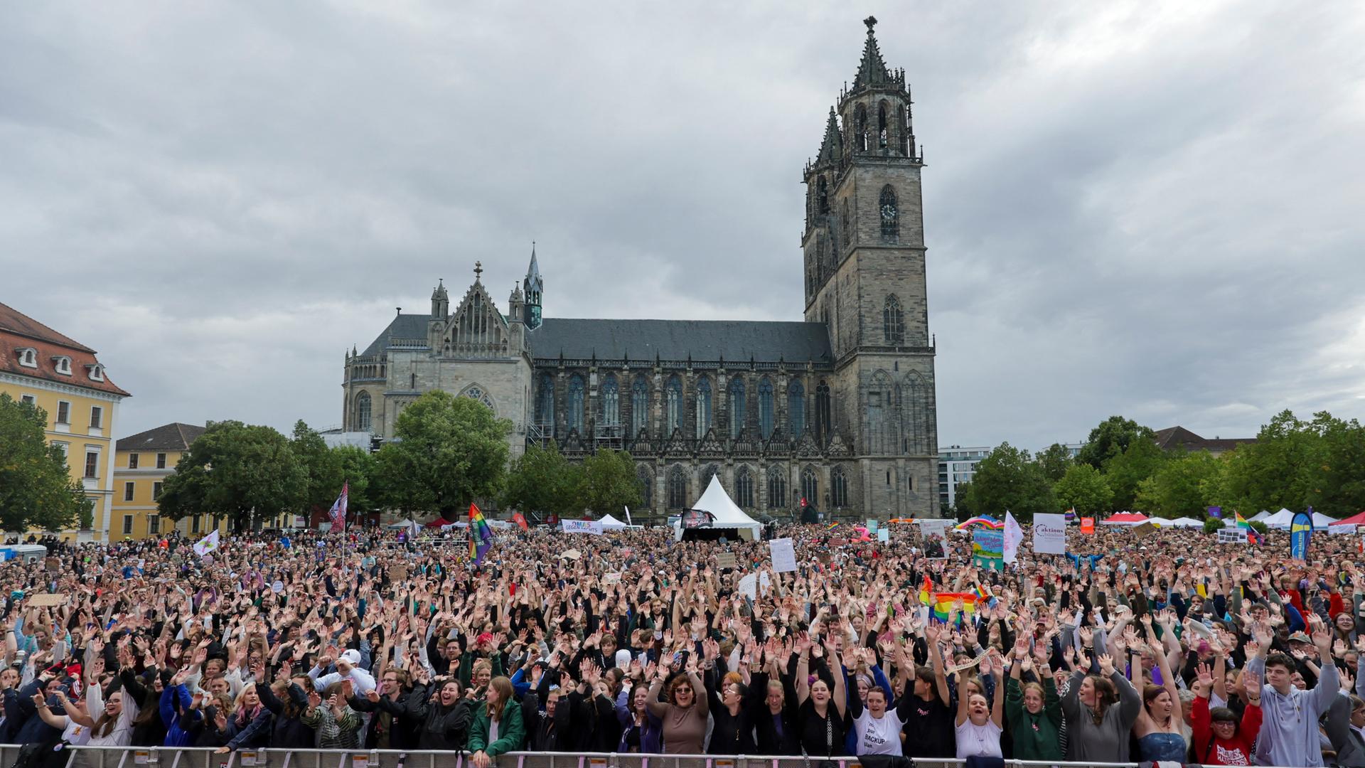 Tausende Menschen stehen auf dem Platz vor dem Magdeburger Dom und recken die Hände in die Höhe. Manche halten Plakate und Regenbogenfahnen in die Höhe. Tausende Menschen stehen auf dem Platz vor dem Magdeburger Dom und recken die Hände in die Höhe. Manche halten Plakate und Regenbogenfahnen in die Höhe.