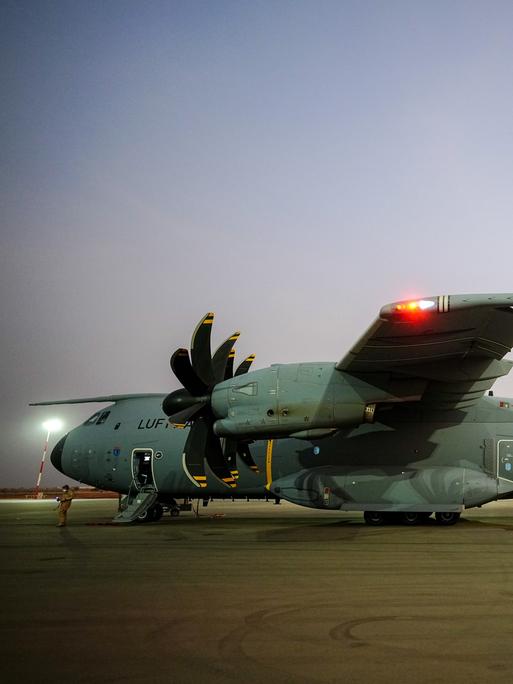 Ein Airbus A400M in der Lackierung der Luftwaffe steht bei Abendlicht auf einem Rollfeld; ein Soldat in khaki-farbener Camouflage läuft auf das Flugzeug zu.