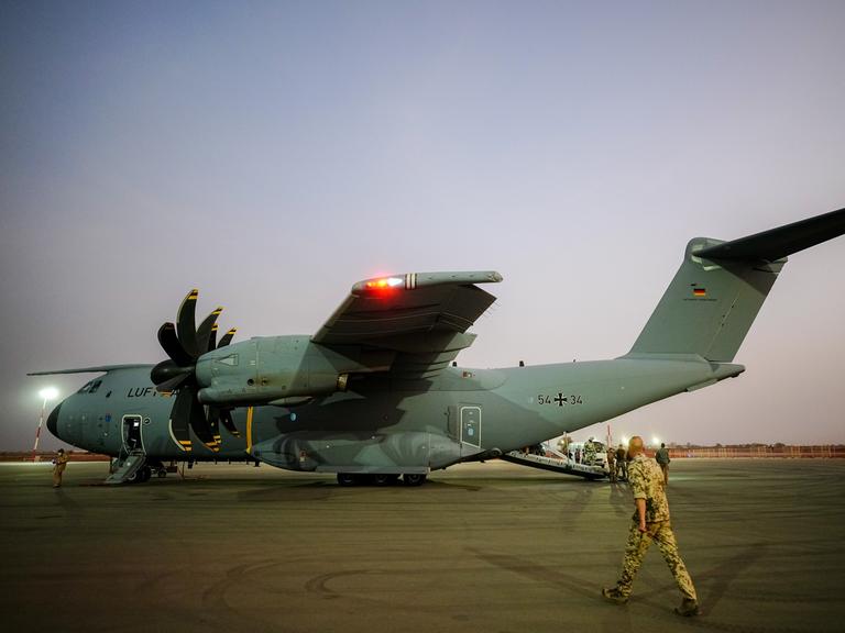 Ein Airbus A400M in der Lackierung der Luftwaffe steht bei Abendlicht auf einem Rollfeld; ein Soldat in khaki-farbener Camouflage läuft auf das Flugzeug zu.