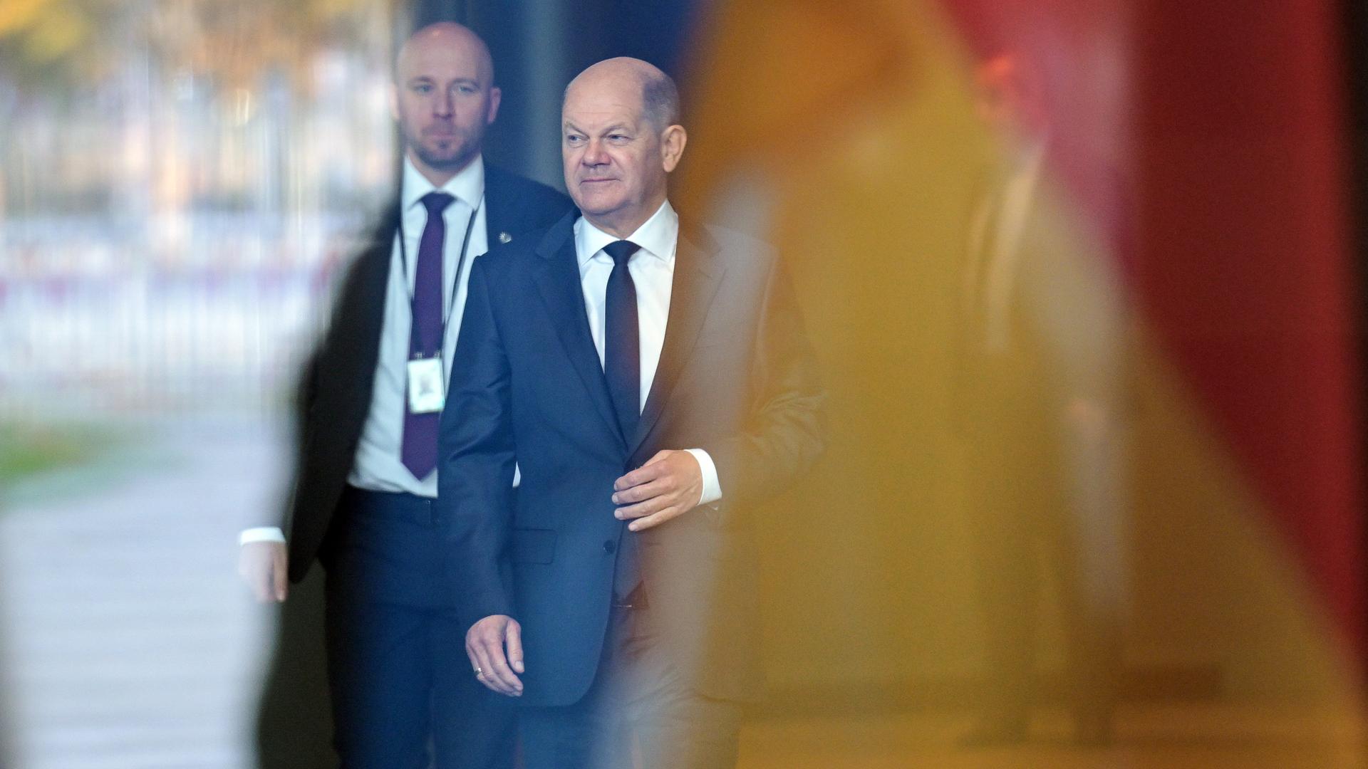 Bundeskanzler Olaf Scholz kommt aus dem Kanzleramt, im Vordergrund verschwommen eine Deutschlandfahne.