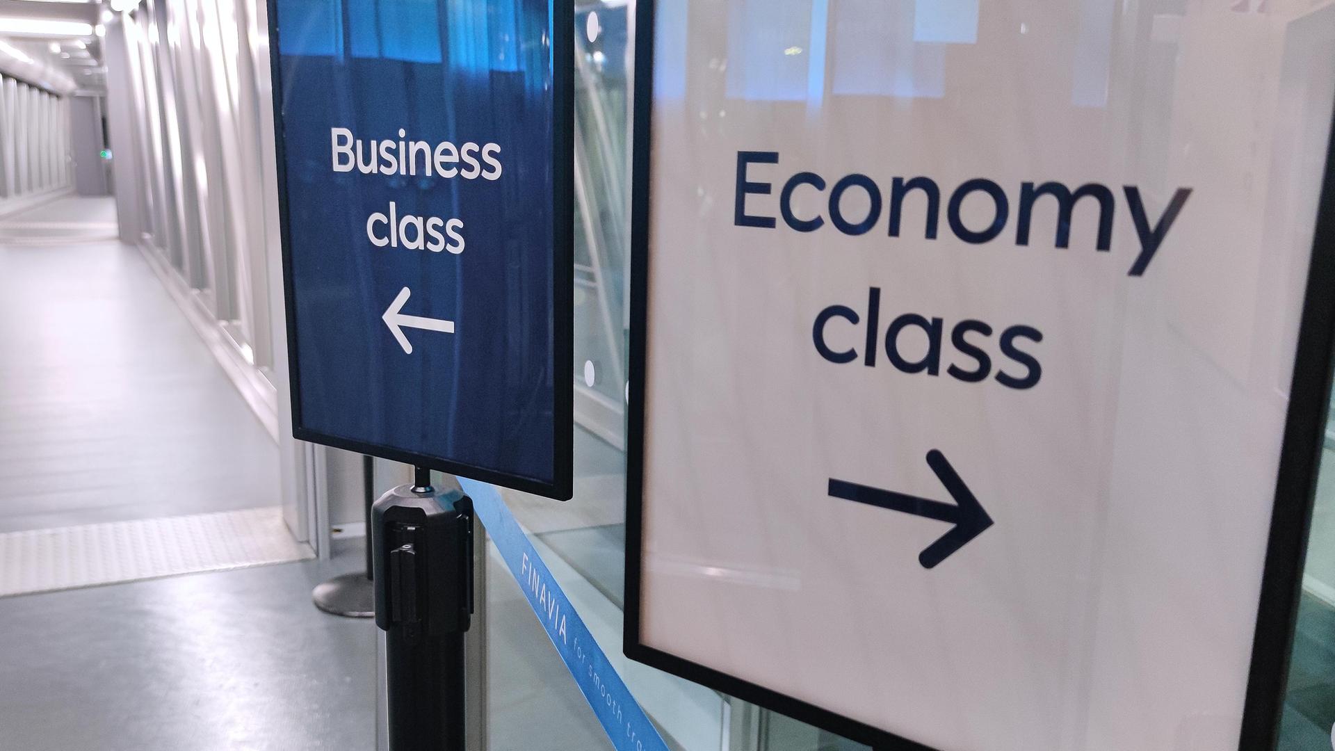 Zwei Wegweiser für Business Class beziehungsweise Economy Class in einer Flughafenhallle.