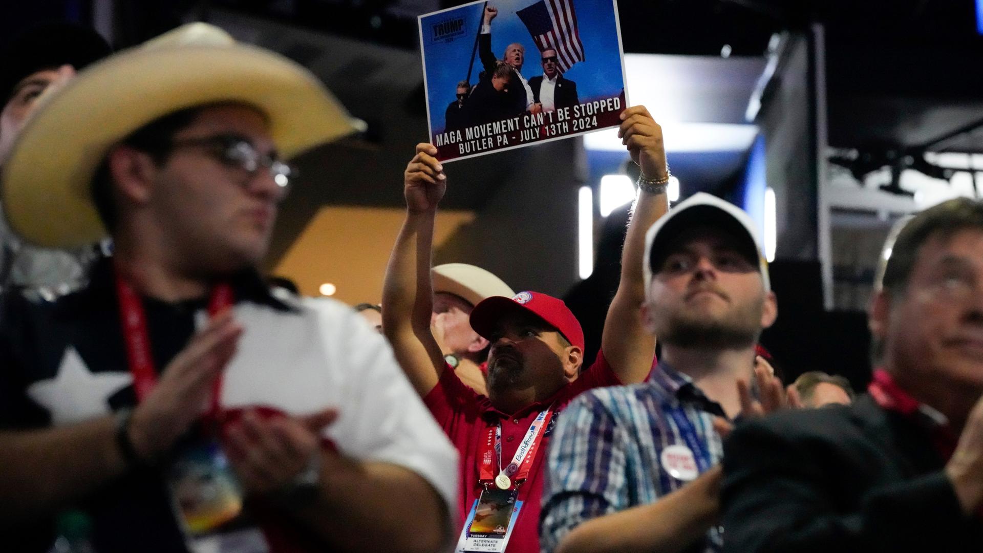 Ein Mann hält in der Menge ein Foto in die Höhe, dass das Bild von Donald Trump kurz nach dem Mordanschlag auf ihn am 13.07.2024 zeigt