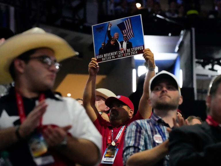 Ein Mann hält in der Menge ein Foto in die Höhe, dass das Bild von Donald Trump kurz nach dem Mordanschlag auf ihn am 13.07.2024 zeigt