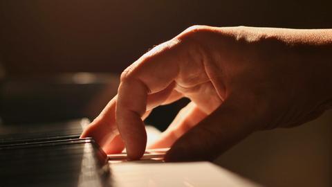 Eine Hand touchiert sanft die Tastatur eines Klaviers.