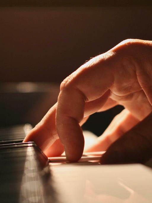 Eine Hand touchiert sanft die Tastatur eines Klaviers.
