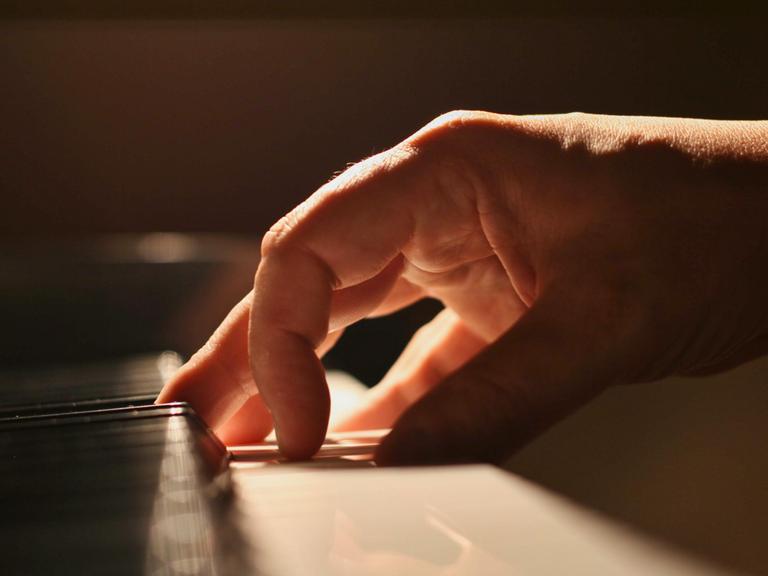 Eine Hand touchiert sanft die Tastatur eines Klaviers.