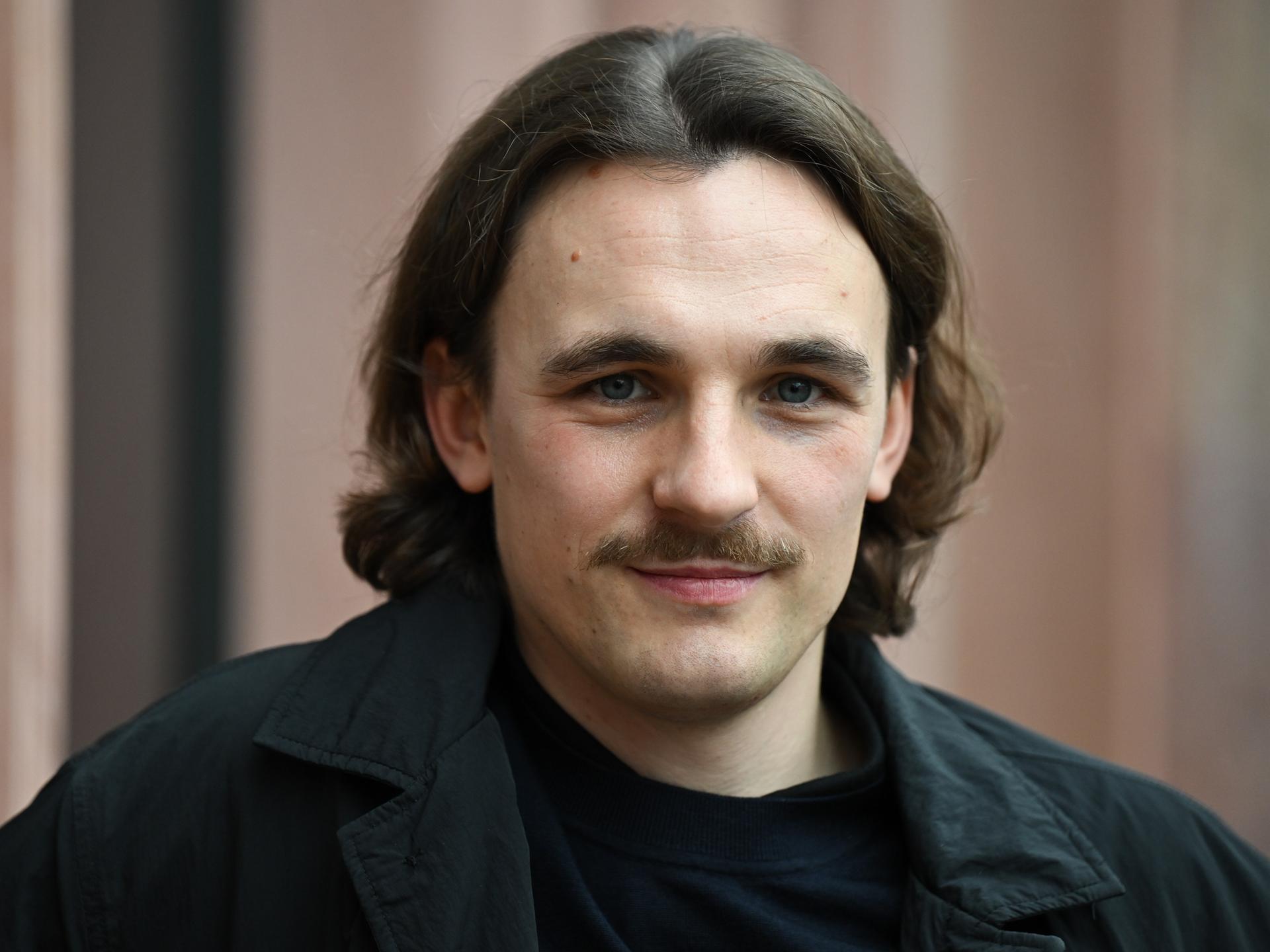 Der Autor Kaleb Erdmann schaut freundlich, mit dunklen Haaren und Schnurrbart. 