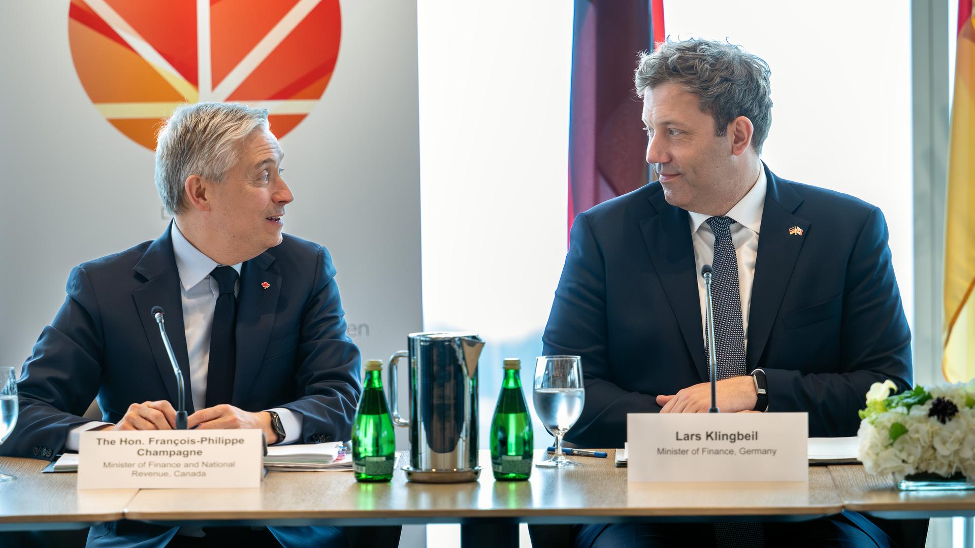 Bundesfinanzminister Lars Klingbeil (r) und sein kanadischer Amtskollege Francois-Philippe Champagne sitzen nebaneinander an einem Tisch und schauen sich freundlich an.