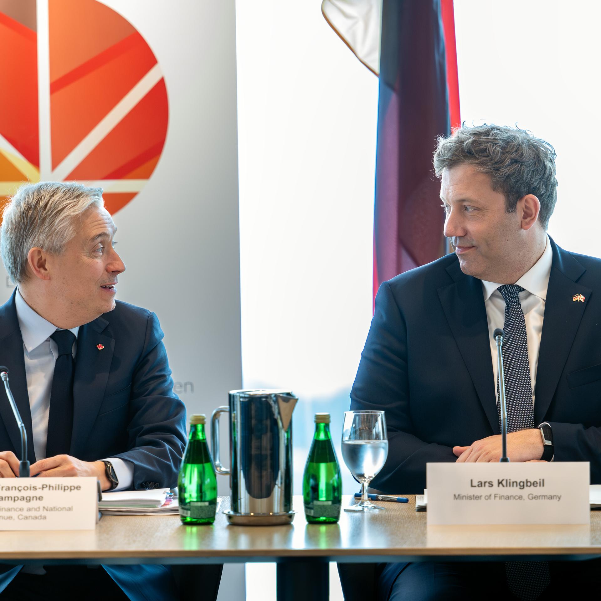 Bundesfinanzminister Lars Klingbeil (r) und sein kanadischer Amtskollege Francois-Philippe Champagne sitzen nebaneinander an einem Tisch und schauen sich freundlich an.
