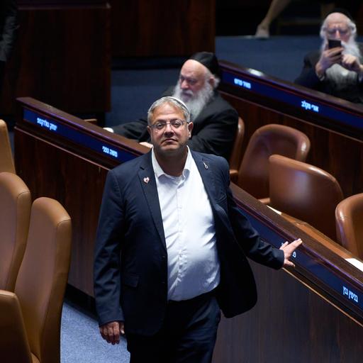 Ben-Gvir steht zwischen den Sitzreihen im israelischen Parlament und schaut in die Kamera.