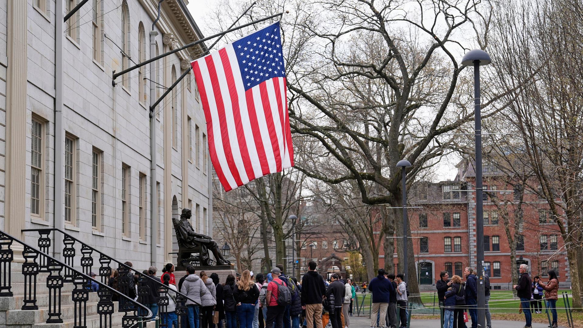 Besucher stehen unter der US-Flagge an der Statue von John Harvard an der Harvard Universität in Cambridge in den USA. Besucher stehen unter der US-Flagge an der Statue von John Harvard an der Harvard Universität in Cambridge in den USA.