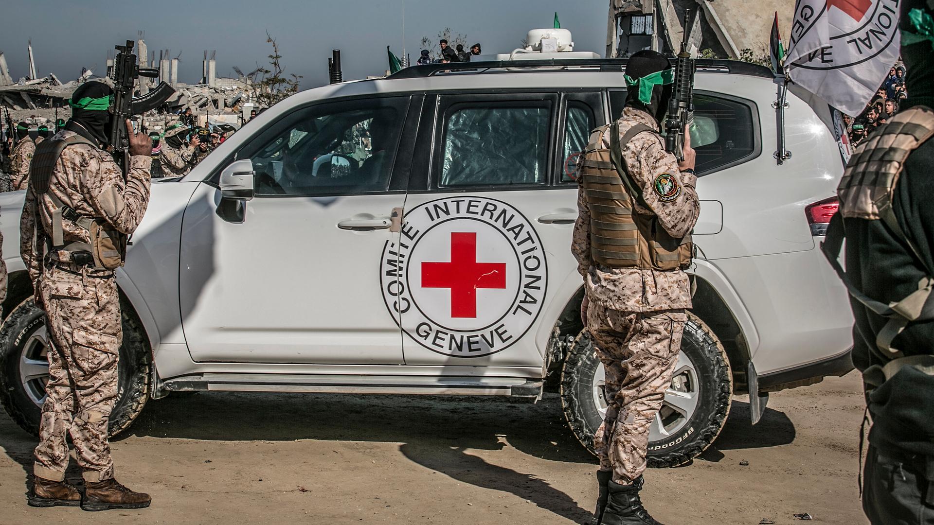 Militate bewaffnete Palästinenser stehen vor einem Fahrzeug des Roten Kreuzes.