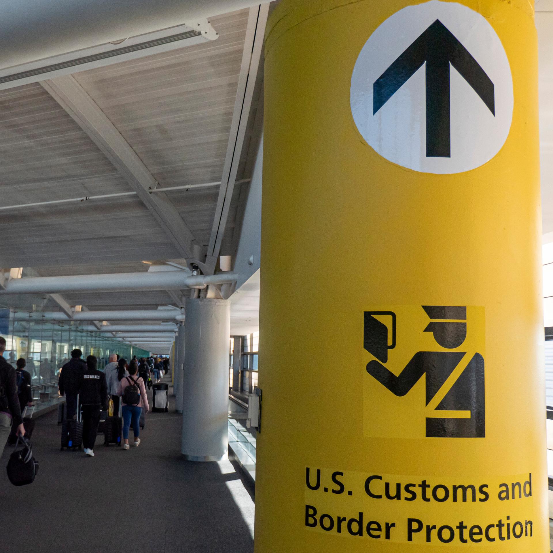 "US-Zoll- und Grenzschutzbehörde" steht auf gelbem Hintergrund im Newark Liberty International Airport (EWR) im Großraum New York. Abgebildet sind zudem ankommende Passagiere. 