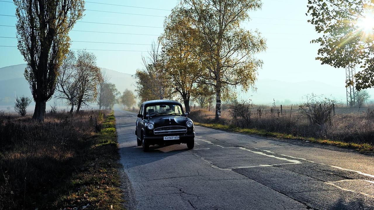 Foto eines alten indischen Autos der Marke Ambassador auf einer baumgesäumten Landstraße Foto eines alten indischen Autos der Marke Ambassador auf einer baumgesäumten Landstraße