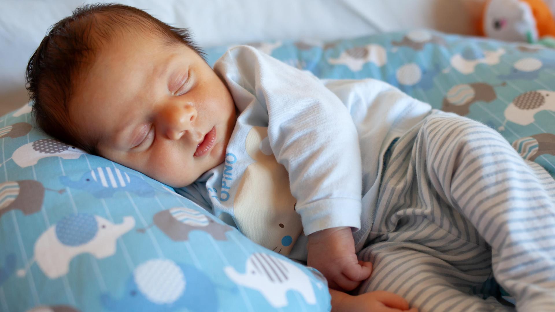 Ein wenige Tage altes Baby schläft auf einem runden Kopfkissen.