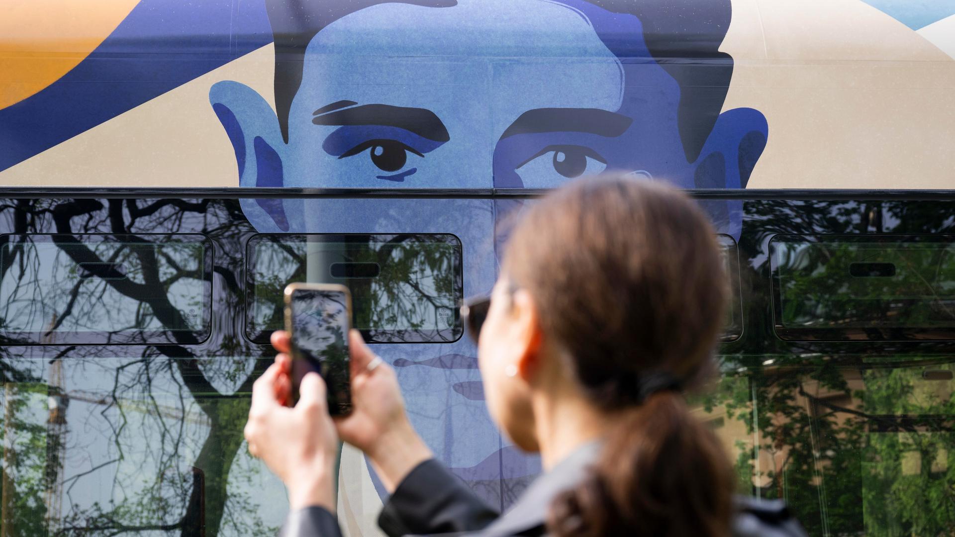Eine Tram in Prag trägt ein Porträt von Franz Kafka. Eine Person davor macht ein Foto davon.