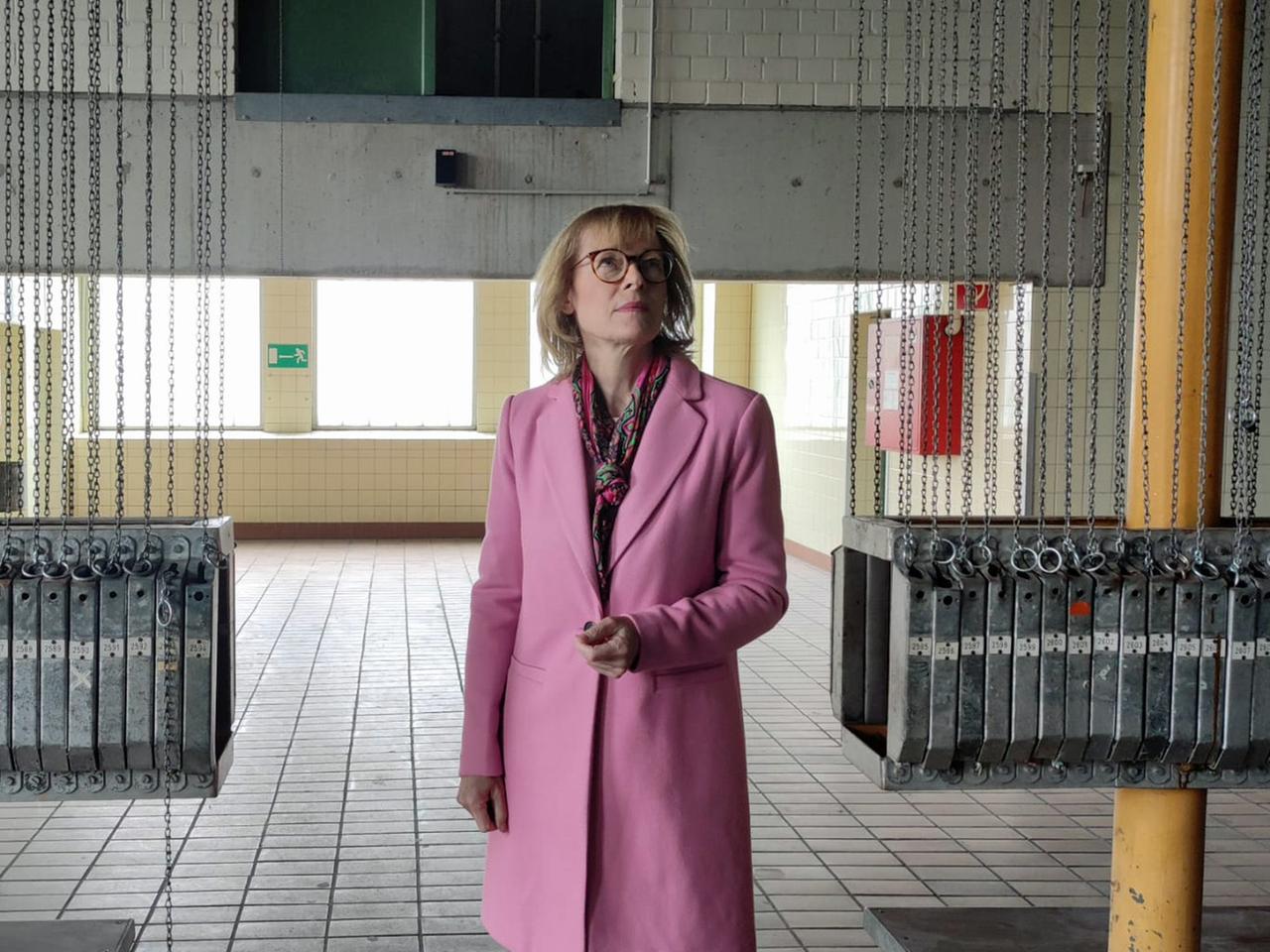 Karin Welge geht mit einem rosafarbenen Mantel durch eine alte Halle