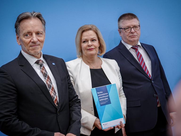 Holger Münch, Nancy Faeser und Thomas Haldenwang stehen nebeneinander auf einer Pressekonferenz und halten eine Broschüre mit der Aufschrift "Rechtsextremismus entschlossen bekämpfen".
