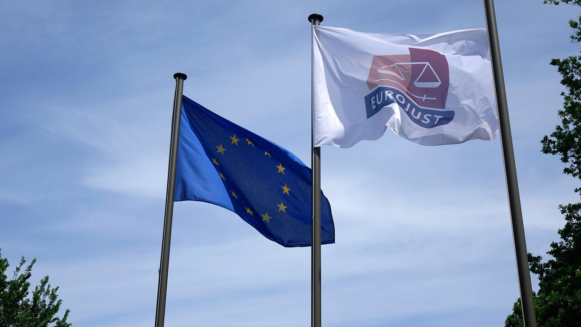 An zwei Fahnenmasten wehen die EU-Flagge und eine Flagge mit dem Logo der EU-Justizbehörde Eurojust. An zwei Fahnenmasten wehen die EU-Flagge und eine Flagge mit dem Logo der EU-Justizbehörde Eurojust.