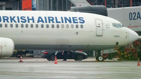 Der Geiselnehmer steigt mit seinem Kind auf dem Arm am Flughafen aus seinem Fahrzeug, das neben einem Flugzeug steht.