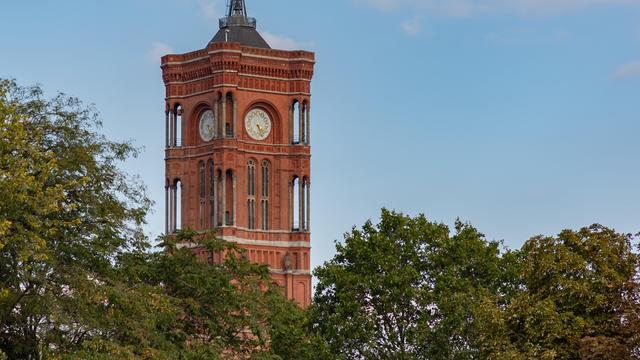 Blick durch grüne Baumkronen auf den Turm des Roten Rathaus.