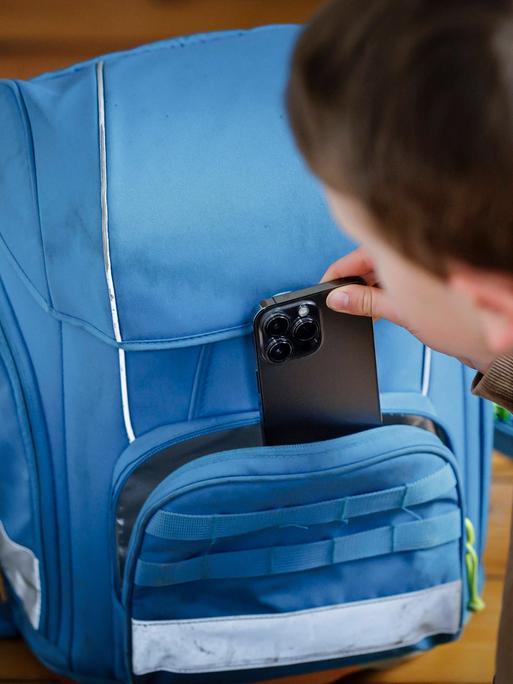 Ein Schulkind holt ein Handy aus seinem Schulranzen.