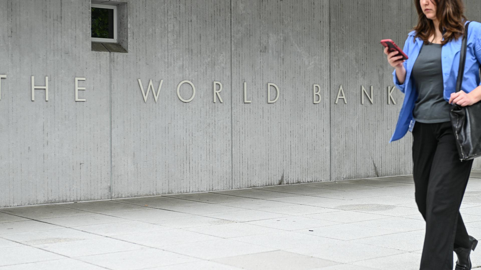 Eine Frau schaut auf ihr Smartphone und geht an einer Betonmauer mit dem Schriftzug "World Bank Group" vorbei, aufgenommen vor der Weltbank-Zentrale in Washington DC.
