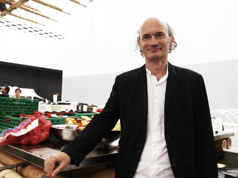 Der Architekt Nikolaus Hirsch steht auf der Art Basel und guckt in die Kamera. Er trägt ein weißes Hemd und eine schwarze Jacke.