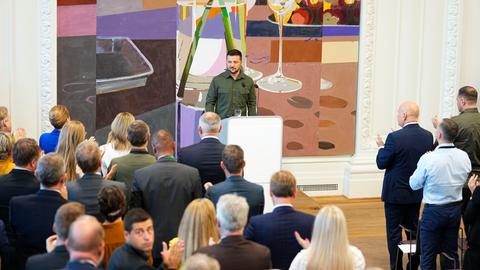 Der ukrainische Präsident Selenskyj spricht im dänischen Parlament vor Abgeordneten. Sie alle stehen und applaudieren ihm.
