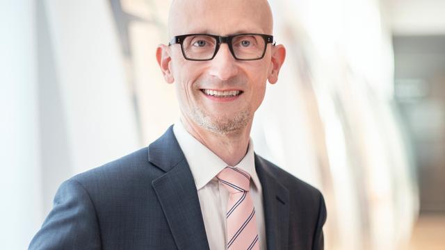 Johannes Neuer, der künftige Direktor der Deutschen Nationalbibliothek in Leipzig, steht vor einer hohen Fensterfront und blickt freundlich in die Kamera.