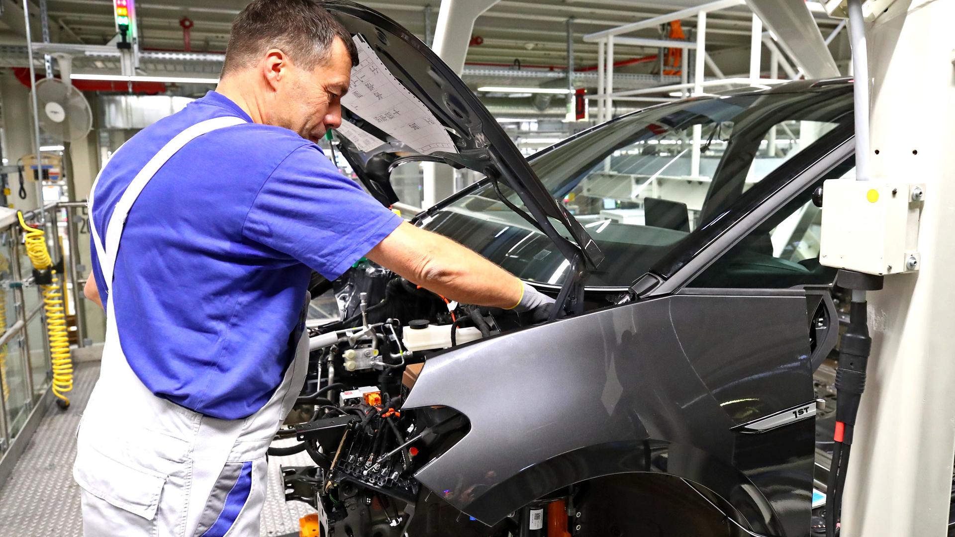 Das Foto zeigt einen Mann in einer Auto-Fabrik. Er baut ein Teil von einem Auto.