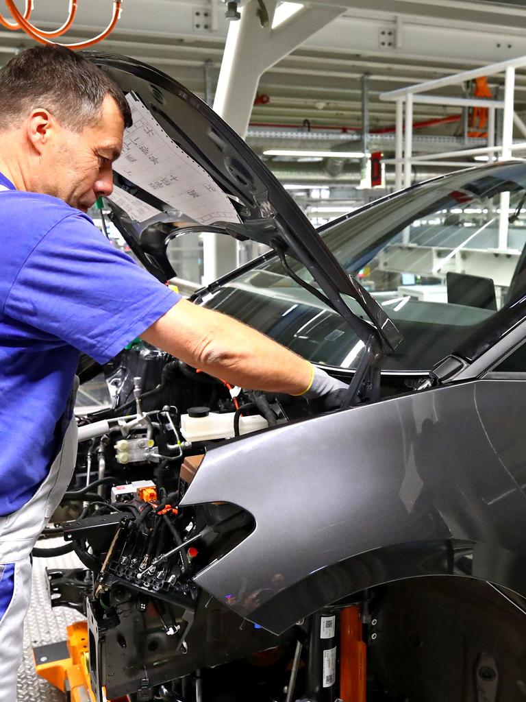 Das Foto zeigt einen Mann in einer Auto-Fabrik. Er baut ein Teil von einem Auto.