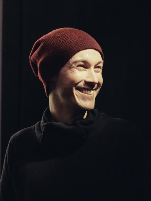 Der Drehbuchautor und Regisseur Benjamin Gutsche im Porträt. Er trägt eine Wollmütze und einen schwarzen Rollkragenpulli und lacht.