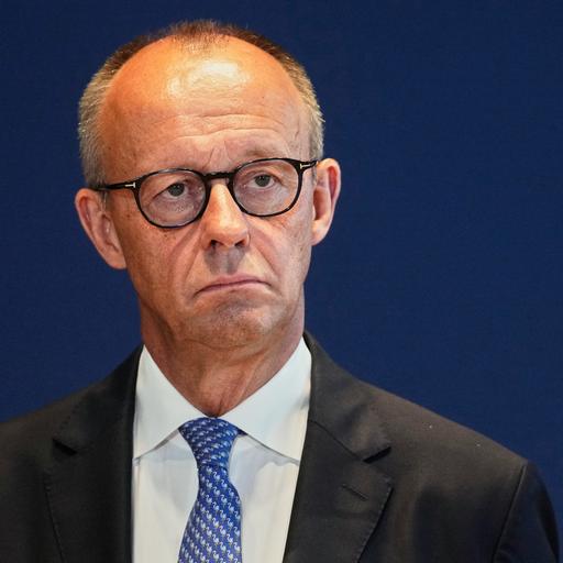 Bundeskanzler Friedrich Merz schaut ernst. Er trägt ein schwarzes Jackett, weißes Hemd und blaue Krawatte. 