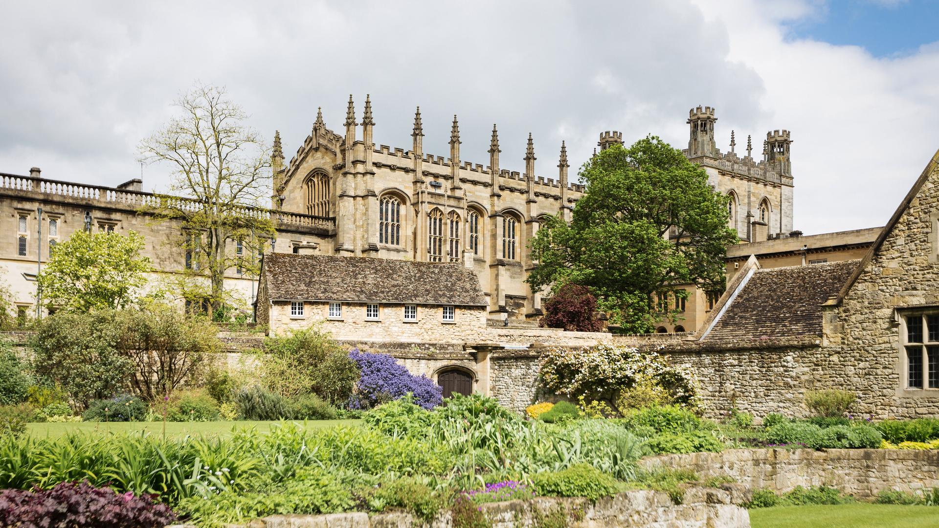 Eine aktuelle Aufnahme zeigt das historische Gebäude des Christ Church College in Oxford inmitten von Blumenrabatten und Bäumen.