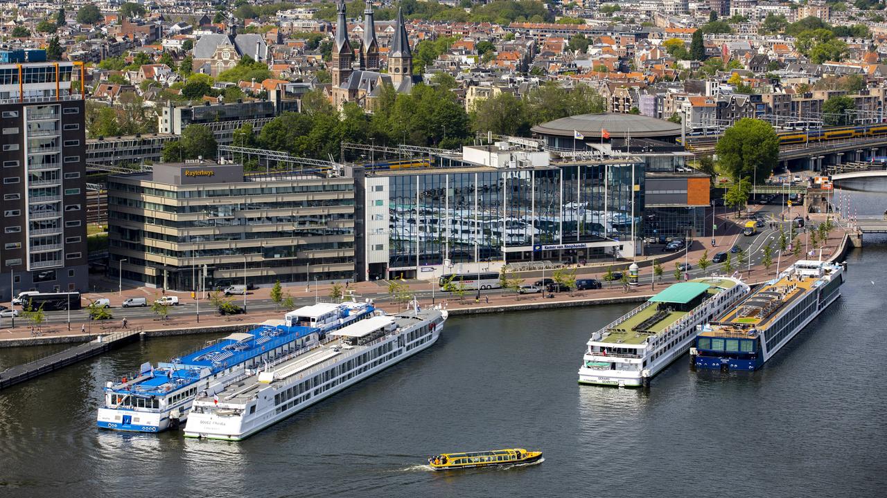 Amsterdam: Flusskreuzfahrtschiffe liegen an einem Pier im Hafen. Im Hintergrund ist die Altstadt aus der Luft zu sehen.