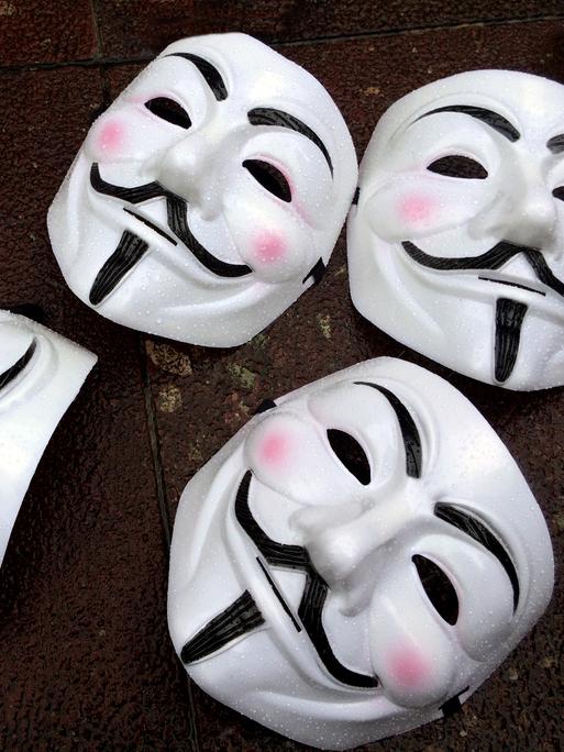 Fünf Guy Fawkes-Masken - weißes Gesicht mit schwarzem Schnurrbart - liegen auf dem Boden. Die Masken sind das Markenzeichen des Hackerkollektivs Anonymous.