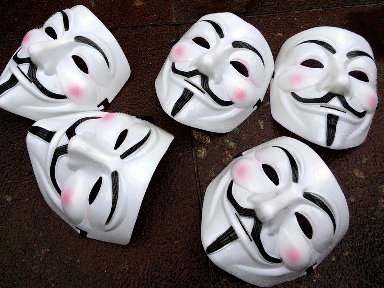 Fünf Guy Fawkes-Masken - weißes Gesicht mit schwarzem Schnurrbart - liegen auf dem Boden. Die Masken sind das Markenzeichen des Hackerkollektivs Anonymous.