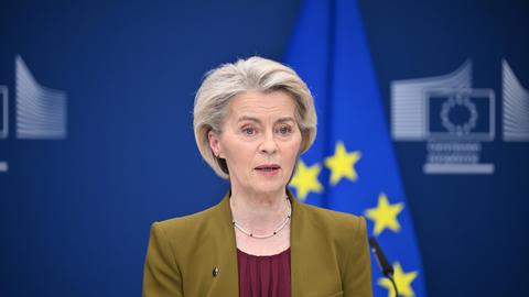 EU-Kommissionspräsidentin von der Leyen steht vor einer verschwommenen EU-Fahne.