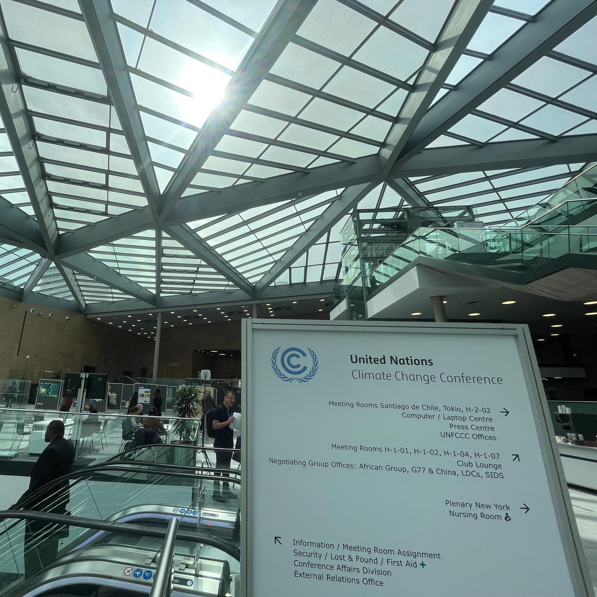 Ein Hinweisschild der UNO-Klimakonferenz steht im Foyer des World Conference Center in Bonn. Danben ist eine Rolltreppe auf der ein Mann nach unten fährt.