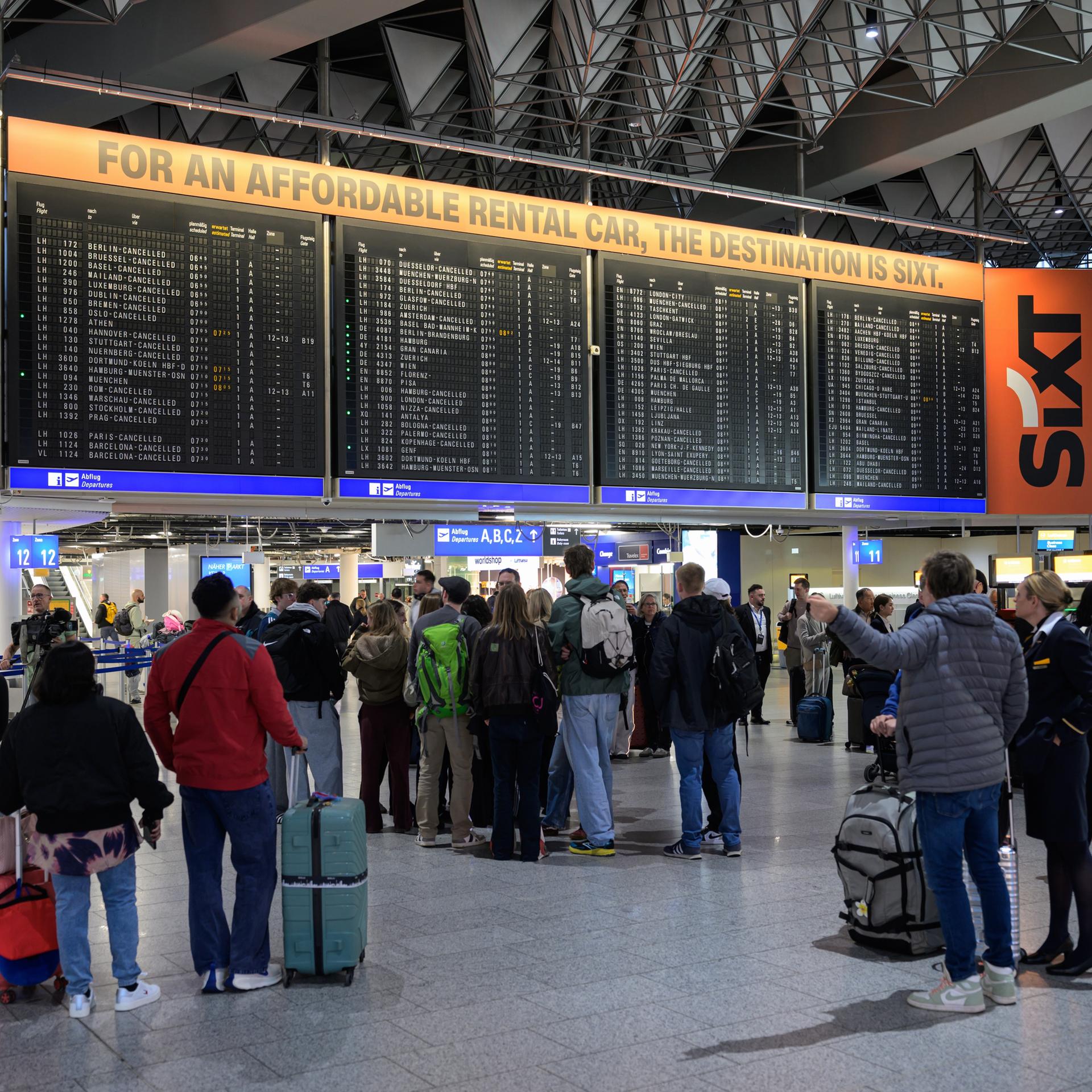 Menschen stehen vor einer Anzeigetafel mit gestrichenen Flügen der Lufthansa am Frankfurter Flughafen.