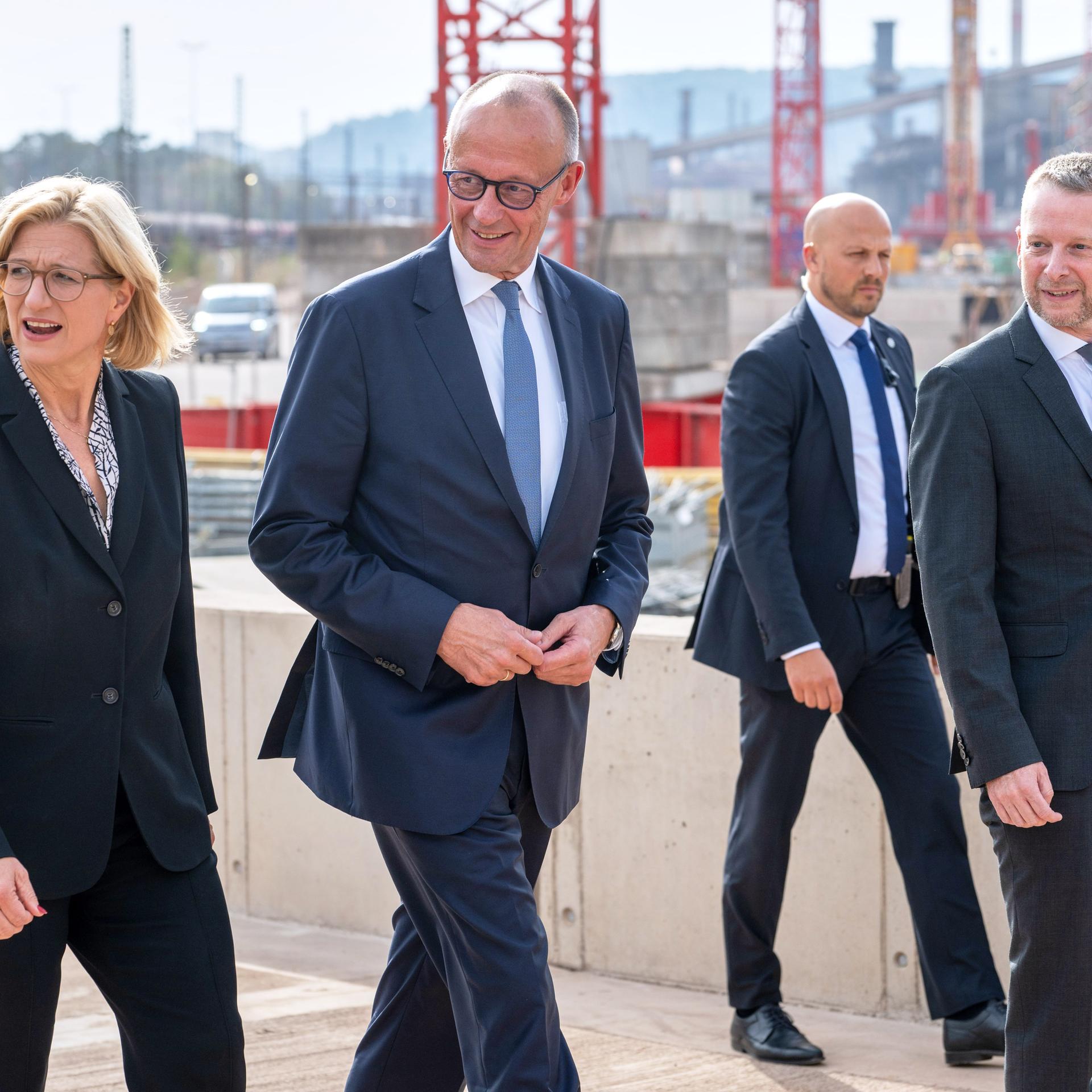Der Vorstandsvorsitzende von Saarstahl Dillinger, Stefan Rauber (r-l), geht mit Bundeskanzler Friedrich Merz (CDU) und der saarländischen Ministerpräsidentin Anke Rehlinger (SPD) über die Baustelle des neuen Werks.