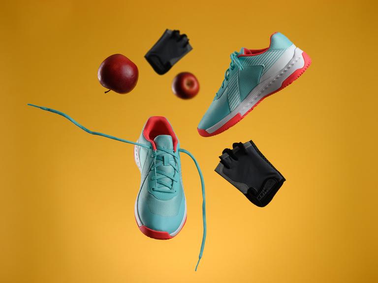 Ein roter Apfel, Handschuhe und ein Paar Turnschuhe fliegen durch die Luft. 