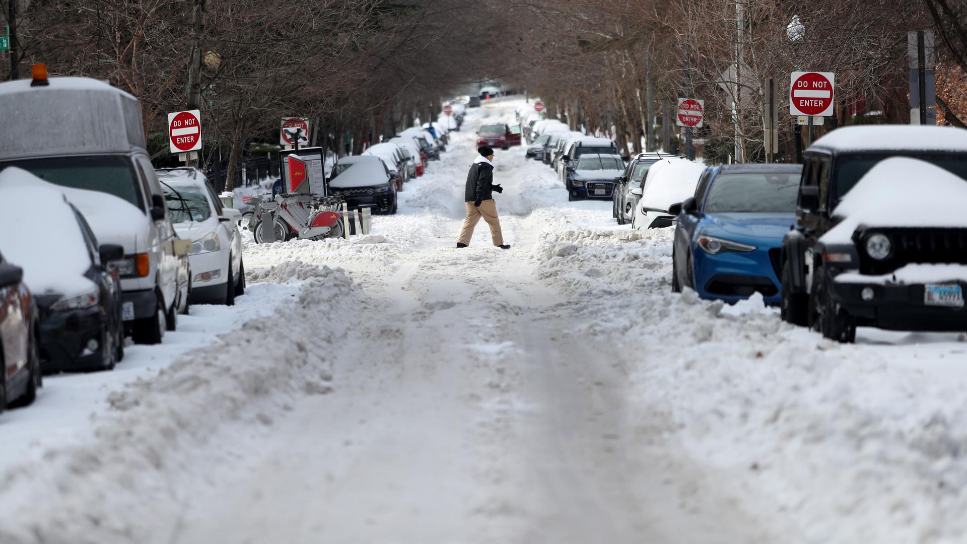 Ein Mann läuft in Washington über eine heftig verschneite Straße, viele Autos stehen am Straßenrand.